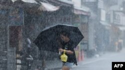 Seorang perempuan tampak berjalan dengan payung di tengah hujan besar yang menggusur wilayah Bandara Su-ao di Yilan saat Badai Haikui melanda wilayah timur Taiwan pada 3 September 2023. (Foto: AFP/I-Hwa Cheng)