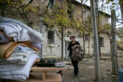 A woman carries her belongings from a damaged house in Thumane, western Albania, Nov. 29, 2019.