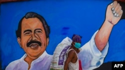 A homeless man wears a face mask against the spread of the new coronavirus, COVID-19, as he walks past a mural depicting Nicaraguan President Daniel Ortega in Managua on April 9, 2020. 