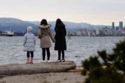 FILE - Maria Law, who emigrated from Hong Kong with her family, views the skyline with her daughters from Jericho Beach in Vancouver, British Columbia, Jan. 26, 2021.