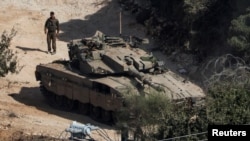 Seorang tentara Israel berdiri dekat tank di tengah bentrokan senjata antara Hizbullah dan Israel di utara Israel, 31 Oktober 2024. Kabinet Israel, Jumat, 1 November 2024, menyetujui anggaran 2025, termasuk kenaikan pajak untuk biayai perang. (Foto: Violeta Santos Moura/Reuters)