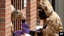 FILE - Specialist team members in military protective suits use a jar in the front doorway as they search the fenced off John Baker House for homeless people in Amesbury, Britain, July 6, 2018. 