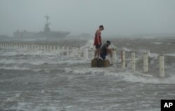 Two men stand near a seawall as Hurricane Hanna makes landfall, July 25, 2020, in Corpus Christi, Texas.
