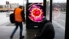 Two men wait at a bus stop with a screen displaying a symbol photo of the novel coronavirus in Berlin, Germany, March 12, 2020.
