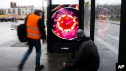 Two men wait at a bus stop with a screen displaying a symbol photo of the novel coronavirus in Berlin, Germany, March 12, 2020.