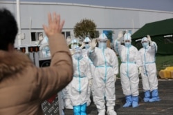 Medical personnel in protective suits wave hands to a patient who is discharged from the Leishenshan Hospital after recovering from the novel coronavirus, in Wuhan in Hubei province, China, March 1, 2020. (Credit: China Daily)