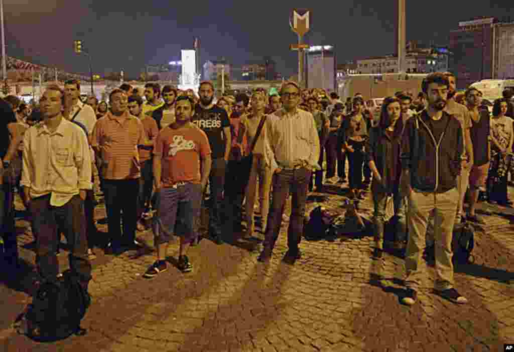Erdem Gunduz, left, and dozens of people stand silently on Taksim Square in Istanbul early Tuesday, June 18, 2013.