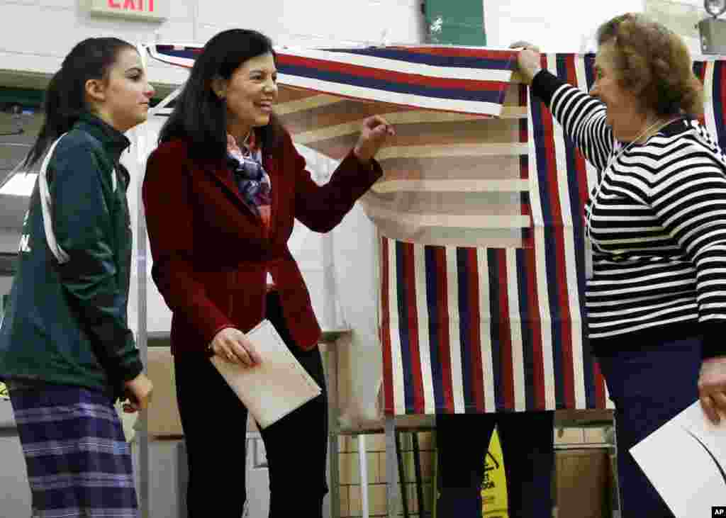 Seorang petugas TPS mengangkat tirai bilik suara saat Senator Kelly Ayotte (tengah) meninggalkan bilik suara bersama putrinya Kate (8/11) di Sekolah Dasar Charlotte Avenue di Nashua, New Hampshire. (AP/Elise Amendola)