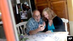Seen through their kitchen window, Allan and Debbie Cameron contact their grandchildren via the internet Wednesday, March 25, 2020, in Chandler, Arizona. Debbie, 68, has asthma which makes her one of the people most at risk from the new coronavirus.