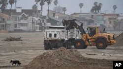 Los equipos de bomberos de la ciudad de Long Beach utilizan excavadoras para mover arena para construir la berma que protege las casas a lo largo de la costa en la Península en Long Beach, California, el lunes 19 de febrero de 2024.