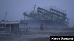 A person reacts to the weather as a ship washed ashore by Typhoon Trami is seen at a port in Yonabaru, on the southern island of Okinawa, Japan, Sept. 29, 2018.