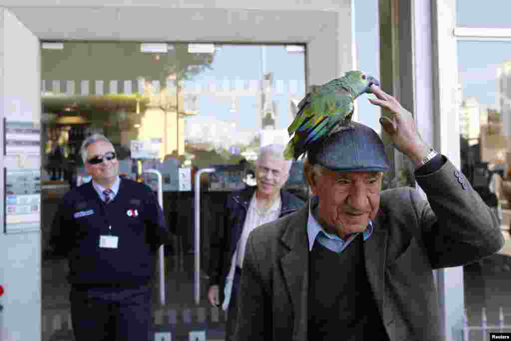 A man walks with a parrot on his hat in front of a Bank of Cyprus branch before it opens in Nicosia, March 28, 2013. 