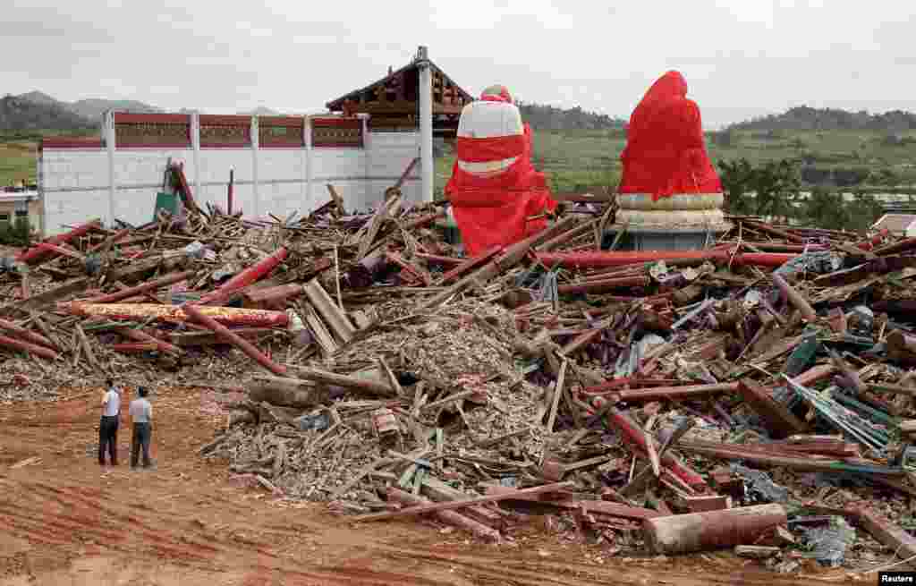 People stand next to debris of a destroyed Buddhist temple under construction and damaged giant Buddha statues after Typhoon Usagi hit Jieshi township of Lufeng, Guangdong province, Sept. 24, 2013.&nbsp;