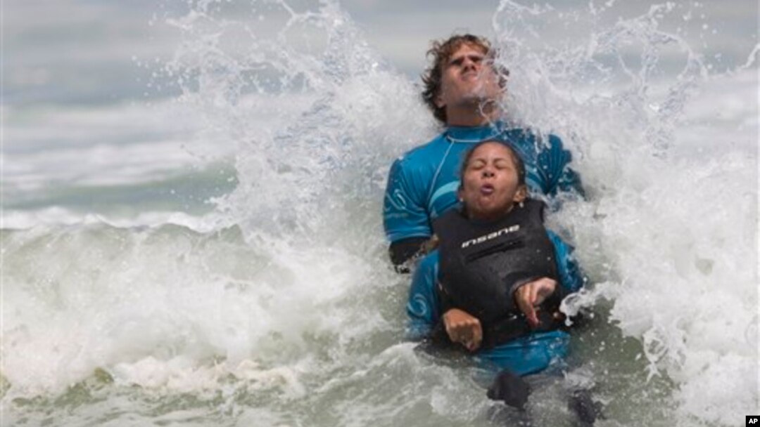Monique Oliveira dibantu oleh relawan AdaptSurf berselancar di pantai Barra da Tijuca di Rio de Janeiro, Brazil. (AP/Felipe Dana)