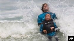 Monique Oliveira dibantu oleh relawan AdaptSurf berselancar di pantai Barra da Tijuca di Rio de Janeiro, Brazil. (AP/Felipe Dana)