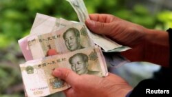 A customer counts Chinese Yuan banknotes as she purchases vegetables at a market in Beijing, China, May 9, 2016. 