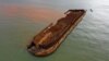 Perahu nelayan di samping tongkang pengangkut nikel yang tenggelam dan mencemari laut di perairan tujuan wisata Pantai Gong di Kabupaten Konawe, Sulawesi Tenggara. (Foto: AFP)