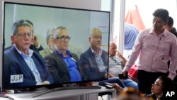 Former leaders of the Revolutionary Armed Forces of Colombia, FARC, Pablo Catatumbo, from left, Rodrigo London, and Carlos Antonio Lozada, are seen on a monitor, during a hearing of the peace tribunal in Bogota, Colombia, July 13, 2018. The FARC leaders have been summoned to the newly created special peace tribunal to respond to war crimes committed during the country's bloody five-decade conflict.