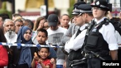 Seorang anak bermain-main dengan pistol-pistolan airnya bersama warga lainnya yang berdiri di belakang garis polisi, saat polisi menggeledah sebuah bangunan di kawasan Barking Road, London timur, 4 Juni 2017.