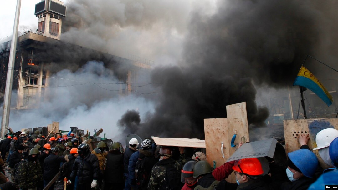 Para demonstran anti-pemerintah di Alun-Alun Kemerdekaan dekat gedung serikat perdagangan yang terbakar di pusat kota Kyiv (19/2). (Reuters/David Mdzinarishvili)