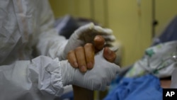 Un trabajador de la salud toma la mano de un paciente con COVID-19 en la unidad de cuidados intensivos del Hospital público Ana Francisca Pérez de León II en Caracas, Venezuela. Marzo 28, 2021.