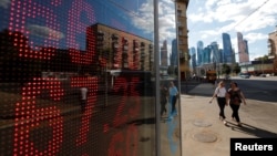 Pedestrians walk past an electronic board showing currency exchange rates of the U.S. dollar and euro against Russian ruble in Moscow, Aug. 10, 2018.