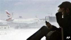 A passenger from San Francisco talks on his phone while a British Airways airplane sits motionless on the runway at John F. Kennedy International Airport in New York, 27 Dec 2010