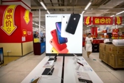 A woman uses her smartphone as she walks past a display for the Apple iPhone XR at a supermarket in Beijing, Tuesday, May 14, 2019. Sending Wall Street into a slide, China announced higher tariffs Monday on $60 billion worth of American goods.