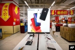 FILE - A woman uses her smartphone as she walks past a display for the Apple iPhone XR in Beijing, May 14, 2019.
