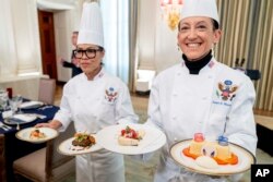 White House executive chef Cris Comerford, left, and White House executive pastry chef Susie Morrison, right, hold dishes during a media preview for the State Dinner with President Joe Biden and French President Emmanuel Macron in the State Dining Room of the White House in Washington, Wednesday, Nov. 30, 2022. (AP Photo/Andrew Harnik)