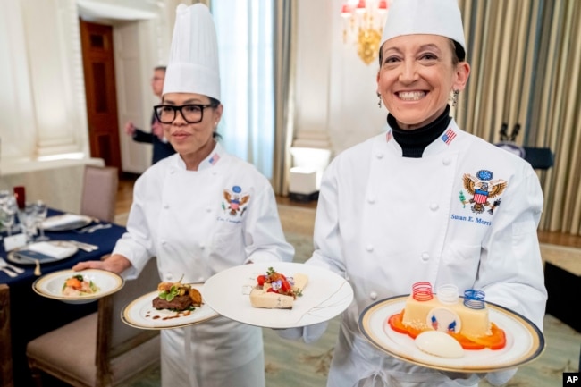 White House executive chef Cris Comerford, left, and White House executive pastry chef Susie Morrison, right, hold dishes during a media preview for the State Dinner with President Joe Biden and French President Emmanuel Macron in the State Dining Room of the White House in Washington, Wednesday, Nov. 30, 2022. (AP Photo/Andrew Harnik)