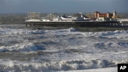 People walks along the shoreline as waves crash onto the beach in Brighton, England, Monday, Oct. 28, 2013. A major storm with hurricane force winds is lashing much of Britain, causing flooding and travel delays with the cancellation of many flights and 