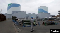 FILE - An employee of Kyushu Electric Power Co walks in front of reactor buildings at the company's Sendai nuclear power plant in Satsumasendai, Kagoshima prefecture.