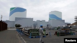 FILE - An employee of Kyushu Electric Power Co walks in front of reactor buildings at the company's Sendai nuclear power plant in Satsumasendai, Kagoshima prefecture.