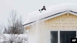 Un hombre usa una pala para quitar la nieve de su techo, el lunes 29 de enero de 2024, en Anchorage, Alaska. Las autoridades han pedido a los habitantes que retiren la nieve de sus techos para que no colapsen.