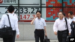 People walk by an electronic stock board of a securities firm in Tokyo. In a report released Sept. 25, 2019, the Asian Development Bank says that escalating trade tensions will sap Asian economies.