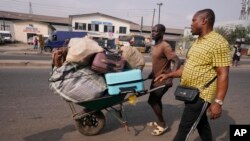 A worker uses a wheelbarrow to carry luggage belonging to passengers traveling for Christmas celebrations, near a bus terminal, in Lagos, Nigeria, Wednesday, Dec. 20, 2023.