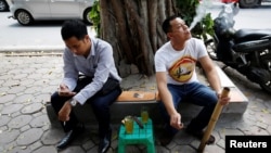 FILE - A man smokes from a bamboo pipe as another holds a cigarette on a street in Hanoi, Vietnam, May 11, 2017.