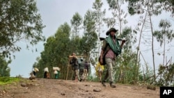 FILE - A militia fighter walks down a path as villagers flee with their belongings in the other direction, near the village of Chenna Teklehaymanot, in the Amhara region of northern Ethiopia, Sept. 9, 2021.