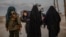 FILE - Veiled women, reportedly wives and members of the Islamic State, walk under the supervision of a female fighter from the Syrian Democratic Forces (SDF) at al-Hol camp in al-Hasakeh governorate in northeastern Syria, Feb. 17, 2019.