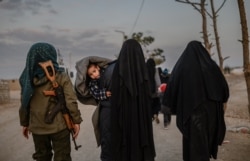 FILE - Veiled women, reportedly wives and members of the Islamic State, walk under the supervision of a female fighter from the Syrian Democratic Forces (SDF) at al-Hol camp in al-Hasakeh governorate in northeastern Syria, Feb. 17, 2019.