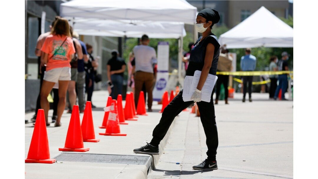 FILE - A medical assistant, right, provides paperwork to people in line at a walk-up COVID-19 testing site in Dallas, Texas, June 11, 2020.