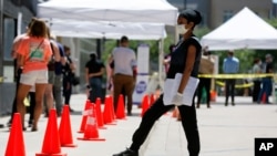 FILE - A medical assistant, right, provides paperwork to people in line at a walk-up COVID-19 testing site in Dallas, Texas, June 11, 2020. 