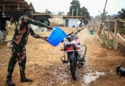 FILE - Motorcycle taxi driver Germain Kalubenge pours chlorinated water on his motorcycle after taking a suspected case of Ebola to an Ebola transit center where potential cases are evaluated, in Beni, Congo, Aug. 22, 2019.