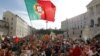 Demonstrators wave a Portuguese flag and shout slogans outside the parliament, at right, during a workers protest, Lisbon, Thursday, March 22, 2012.