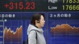 A woman walks by an electronic stock board of a securities firm in Tokyo, Feb. 1, 2016. Chinese stocks fell Monday after a weak manufacturing report. Other markets were mixed. 