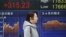 A woman walks by an electronic stock board of a securities firm in Tokyo, Feb. 1, 2016. Chinese stocks fell Monday after a weak manufacturing report. Other markets were mixed. 