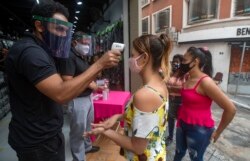 A mask-wearing shopper gets her temperature checked before entering a store in a downtown shopping district in Sao Paulo, Brazil, June 10, 2020.