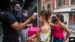 A mask-wearing shopper gets her temperature checked before entering a store in a downtown shopping district in Sao Paulo, Brazil, June 10, 2020. 