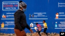 People walk past a COVID-19 advertisement in the township of Soweto outside of Johannesburg, South Africa, July 13, 2020.